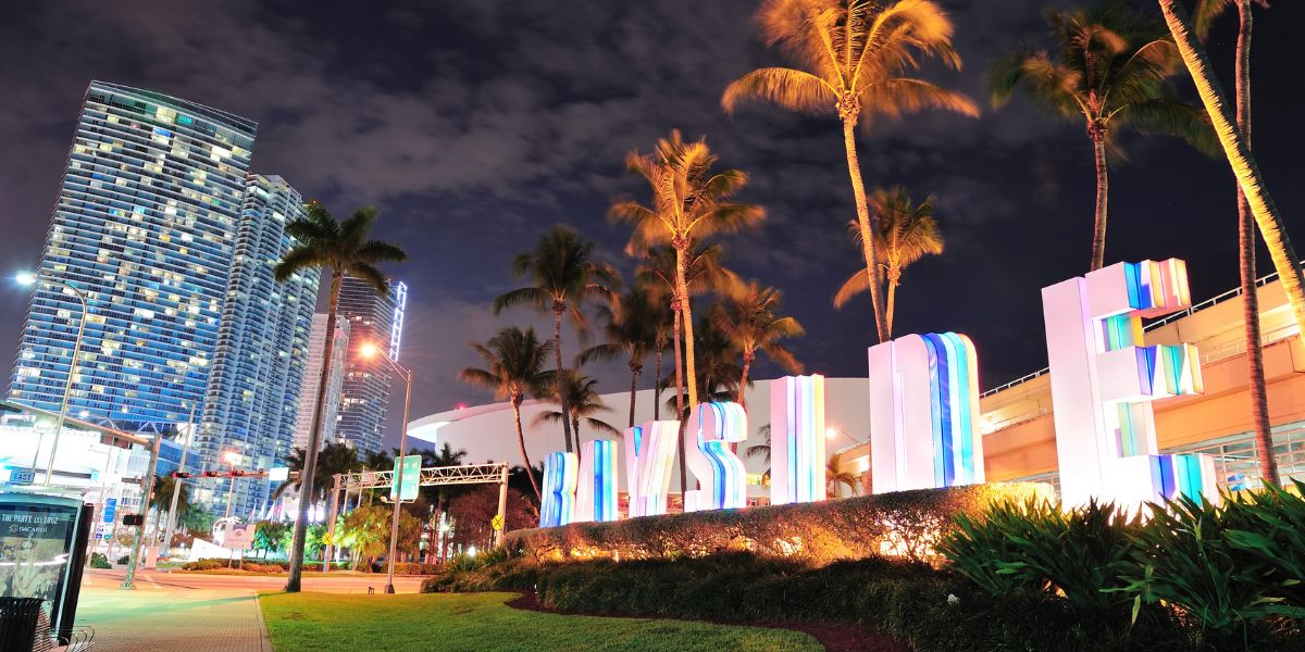 Illuminated Bayside Marketplace sign surrounded by palm trees at night